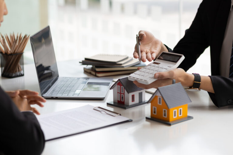 Personne utilisant une calculatrice à côté d'une maquette de maison, symbolisant le calcul de la durée idéale pour un prêt immobilier.