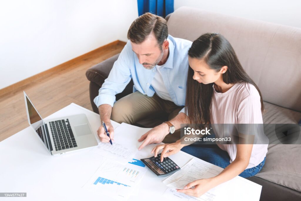Couple consultant un contrat de prêt avec calculatrice et ordinateur, symbolisant l’apport personnel dans un crédit immobilier.