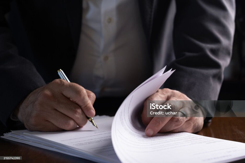 Main signant un contrat immobilier avec un stylo sur un bureau en bois, symbolisant les frais de notaire lors d’un achat immobilier.