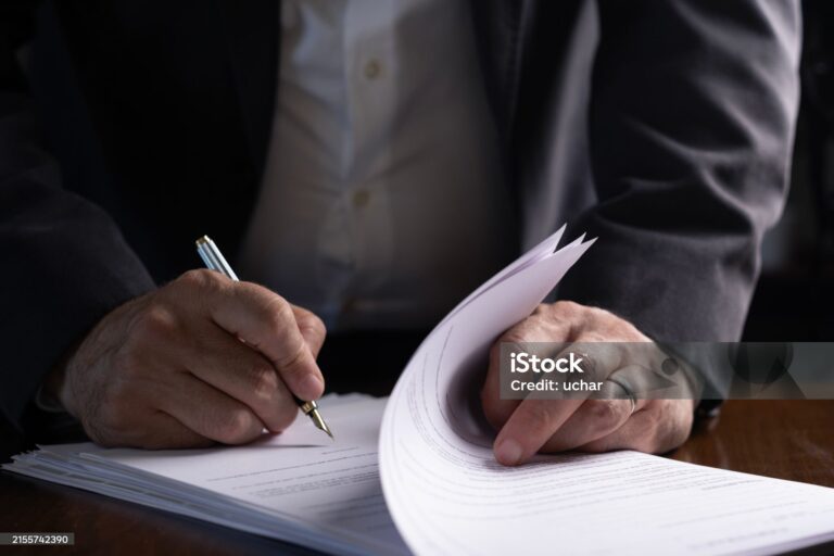 Main signant un contrat immobilier avec un stylo sur un bureau en bois, symbolisant les frais de notaire lors d’un achat immobilier.
